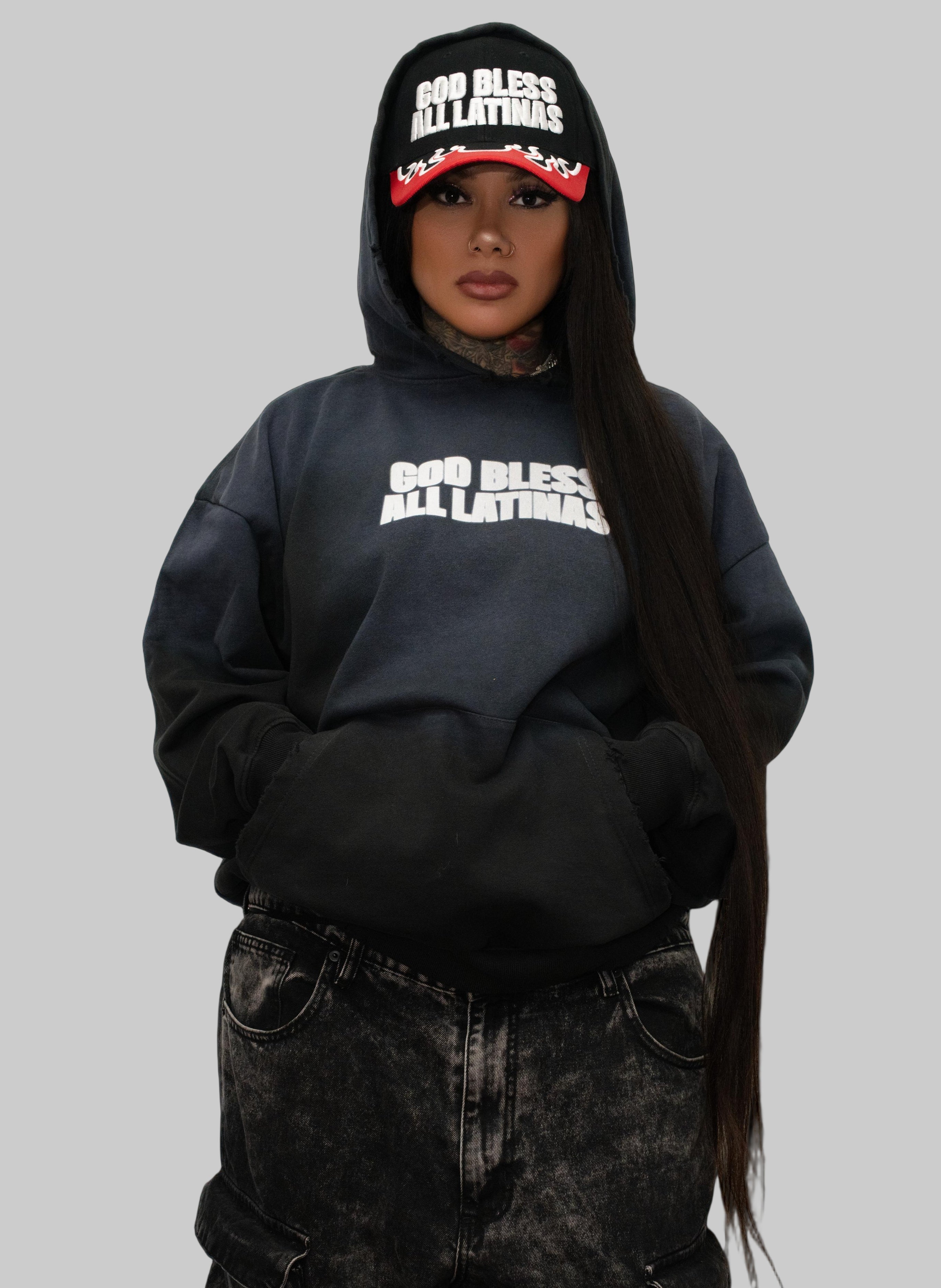 Person wearing a black hoodie with text and matching pants against a white wall.